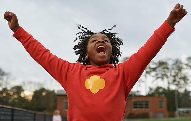 young girl scout outside cheering with hands in the air